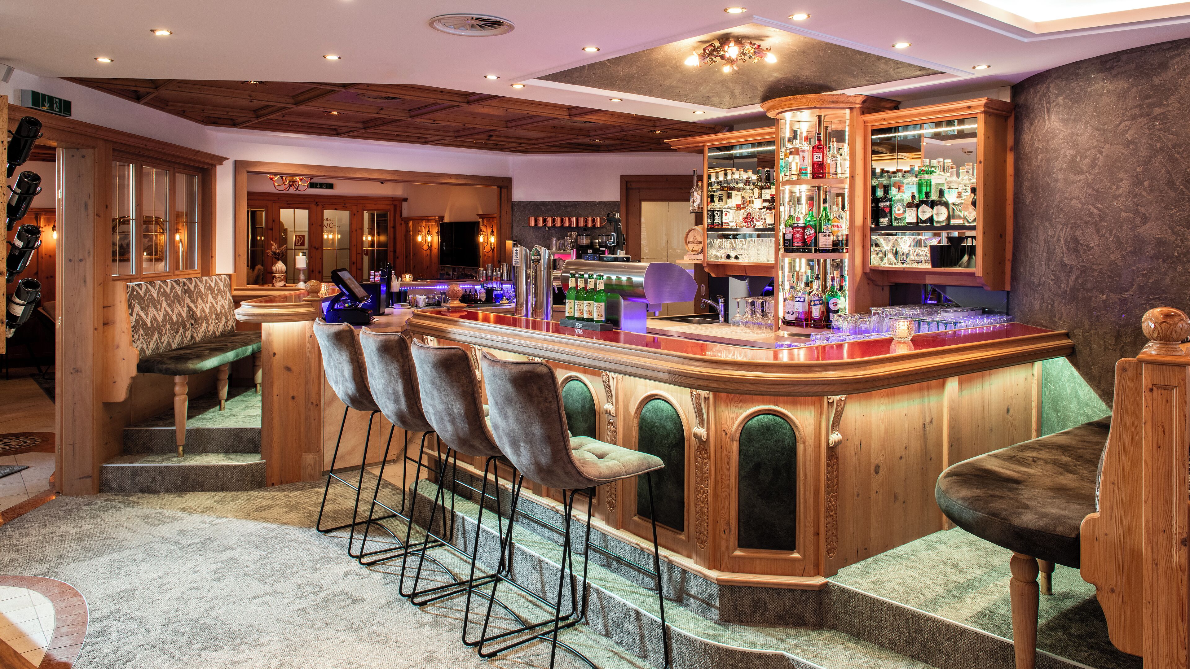 Una zona de bar con mostrador de madera, varios taburetes y una variedad de botellas de licor.