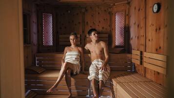 Dos personas en una sauna con bancos de madera y ventanas de celosía.