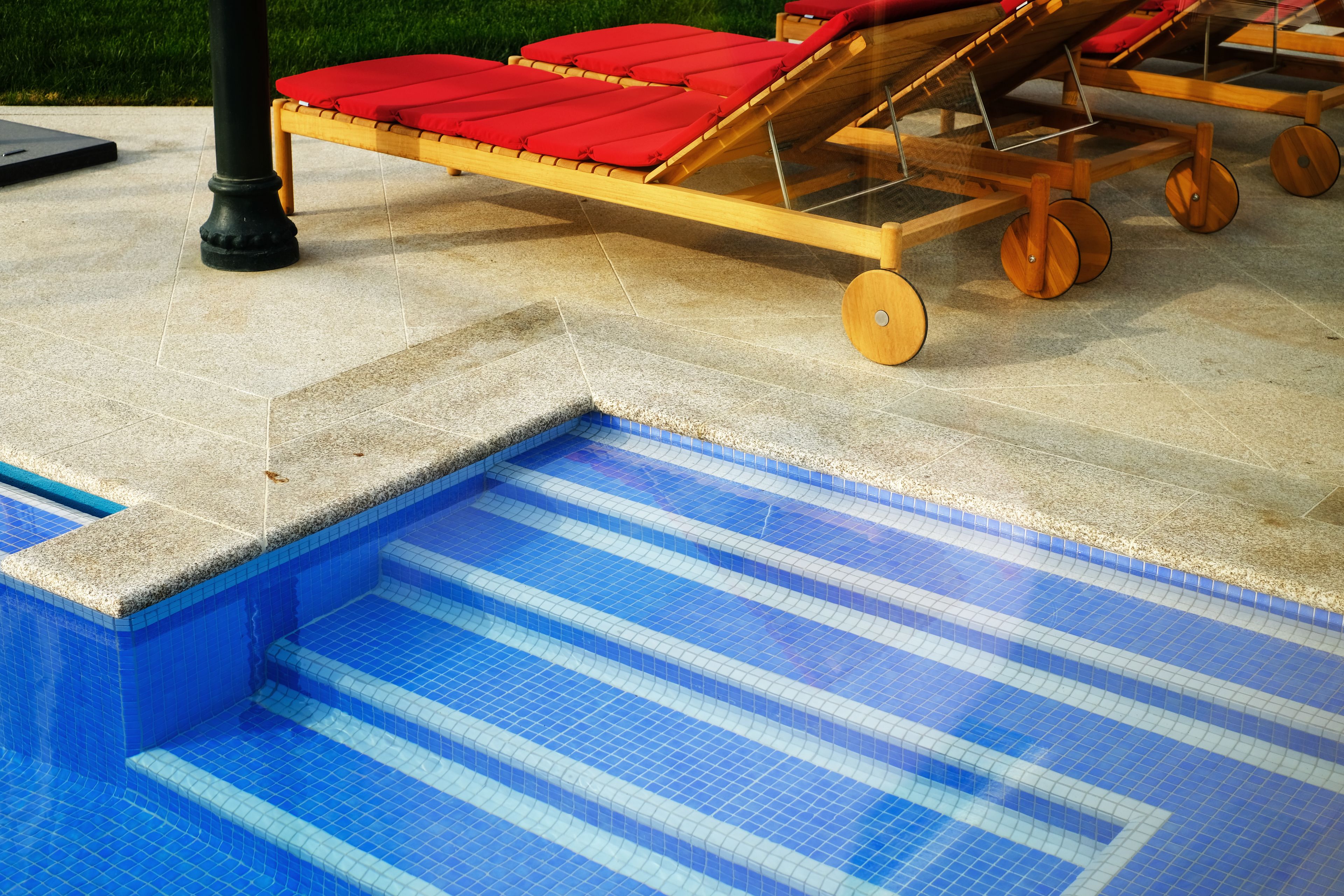 Un área de piscina con una terraza de madera y sillas de descanso rojas.