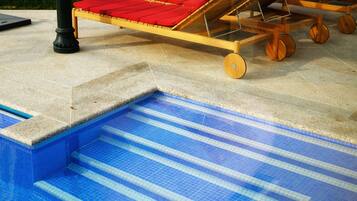 Un área de piscina con una terraza de madera y sillas de descanso rojas.