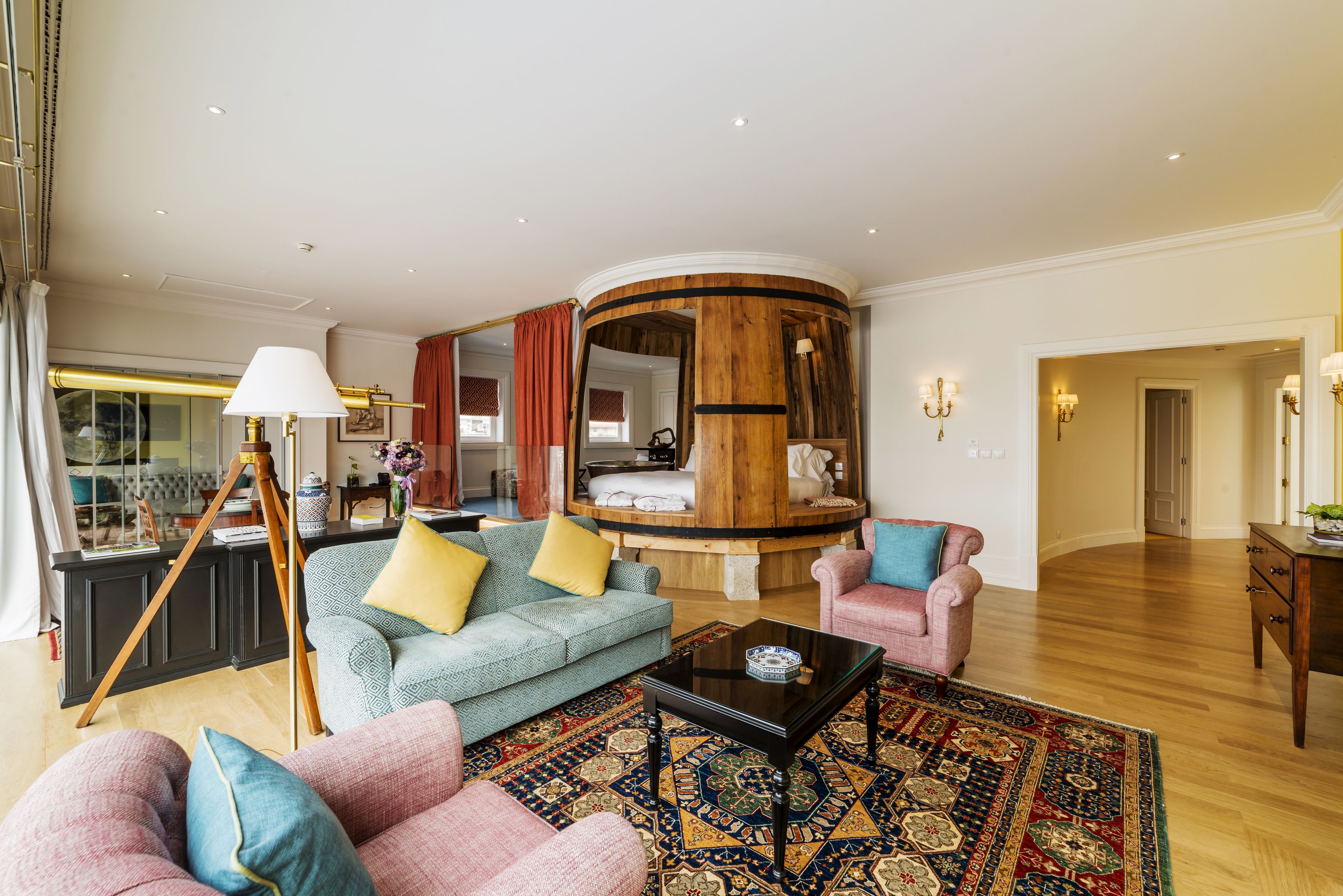 A spacious living area with a round wooden structure, a blue sofa with yellow cushions, a pink armchair, and a coffee table.
