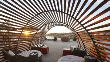 A rooftop terrace with a curved metal roof, wicker furniture, and a view of the cityscape.