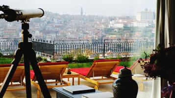 A balcony with a telescope, lounge chairs, and a view of a cityscape.