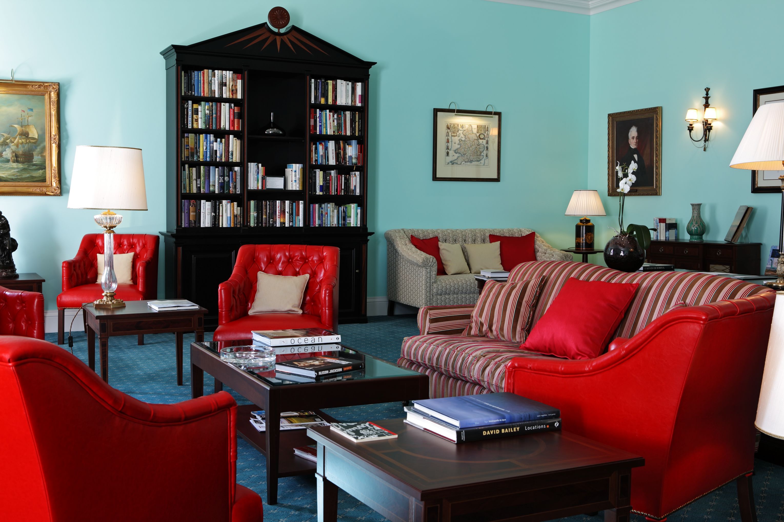 Un salon avec une grande bibliothèque, des fauteuils en cuir rouge, un canapé à rayures et une table basse sur laquelle sont posés des livres.