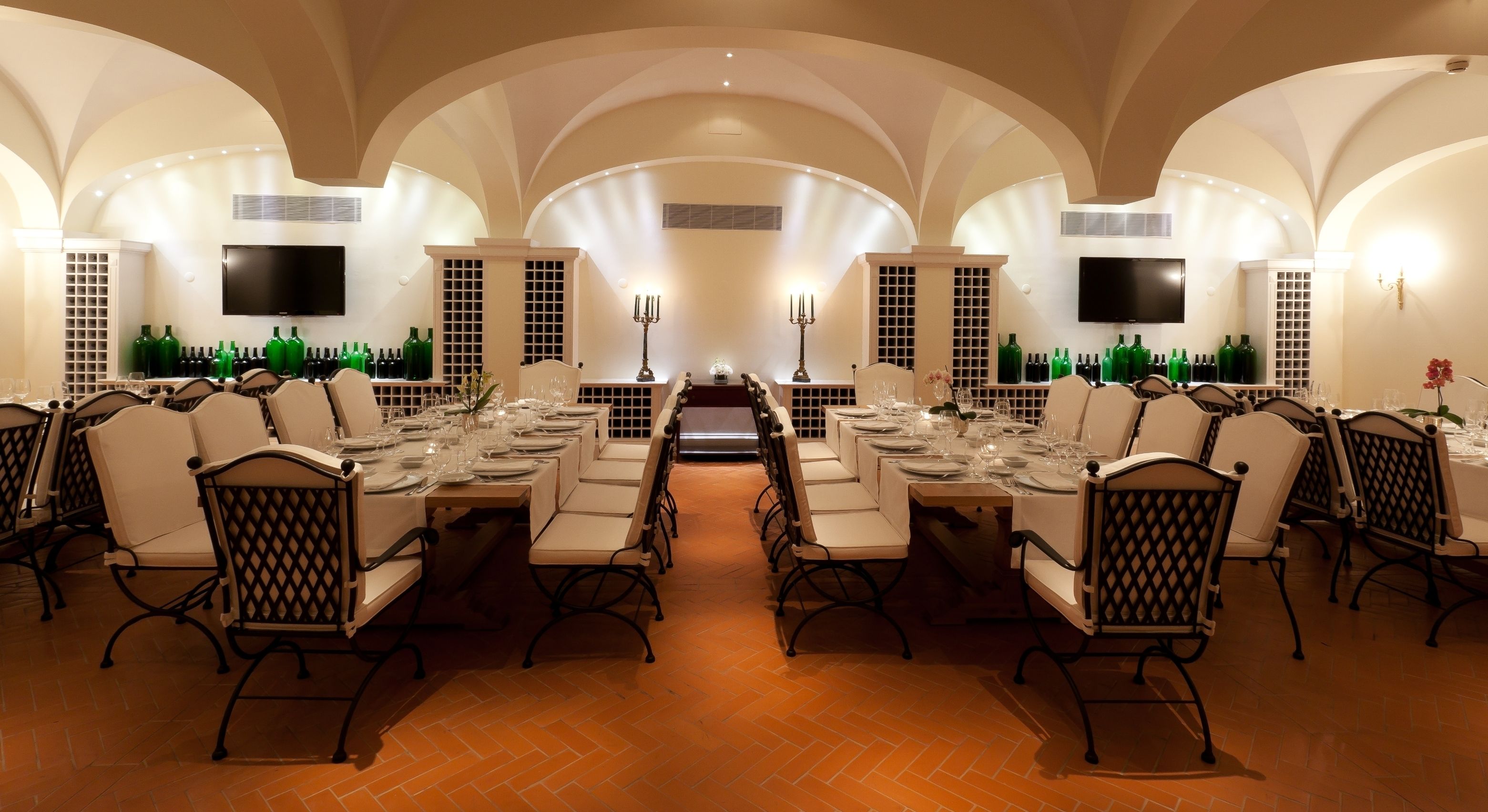 Un comedor formal con una larga mesa dispuesta para una comida, flanqueada por sillas con un diseño de respaldo de celosía, y un piso de baldosas.
