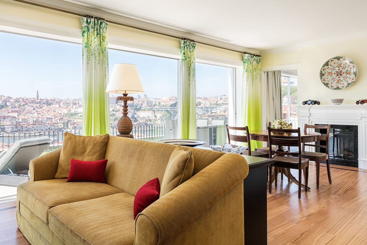 Un salon comprenant un canapé, une table à manger avec des chaises, une cheminée et une vue sur le paysage urbain, visible à travers de grandes fenêtres.