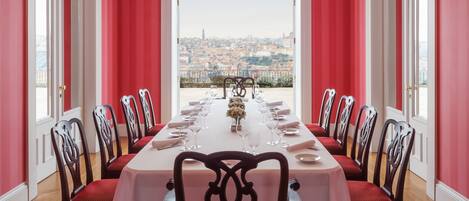 Una sala da pranzo con un lungo tavolo apparecchiato per un pasto, affiancato da sedie, con vista sulla città attraverso un'ampia finestra.