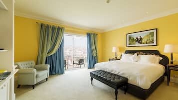 Una habitación de hotel con una cama, una silla, un banco, un escritorio y un balcón con cortinas.