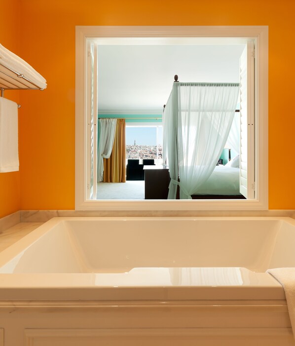 Un baño moderno con una bañera grande, vistas de la ciudad a través de una ventana y una cama con dosel.
