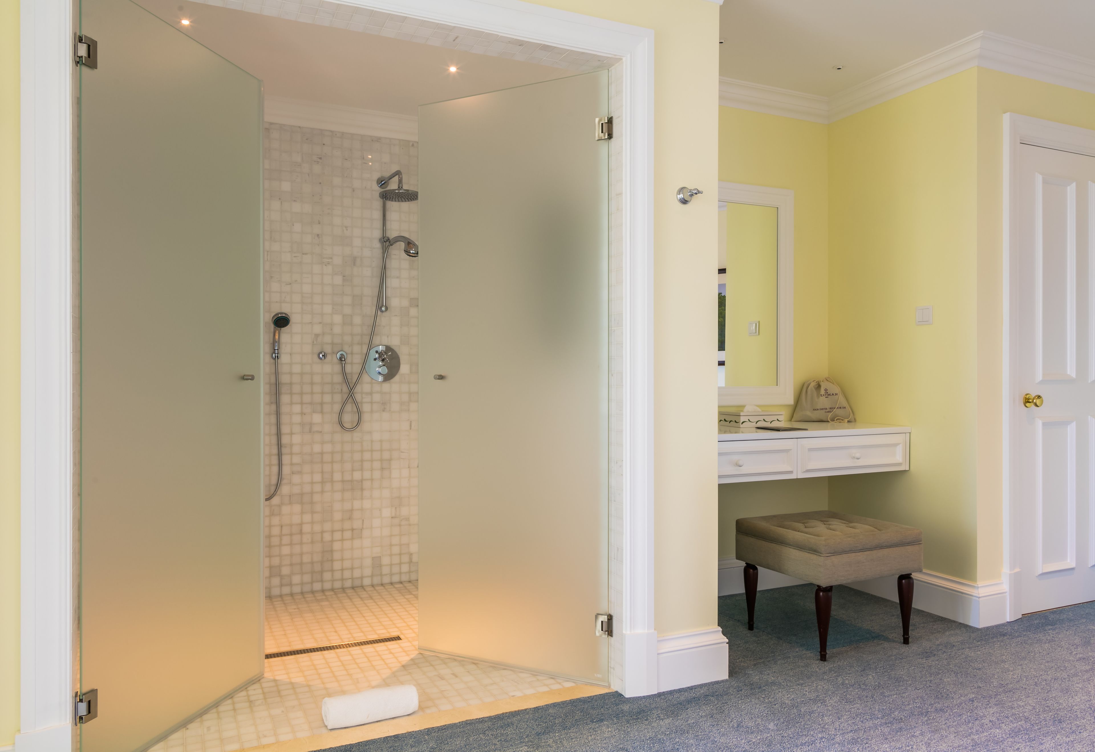 A bathroom with a shower, a vanity with a mirror, and a bench.