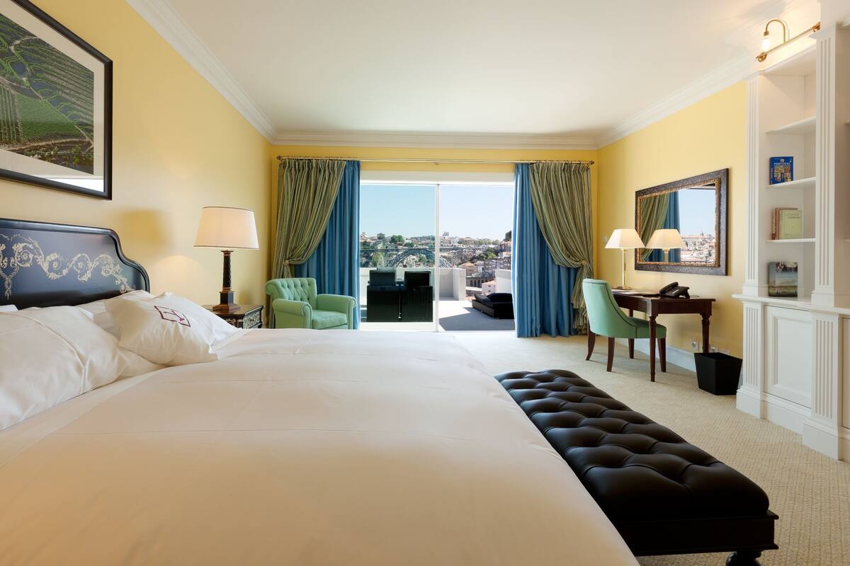 Une chambre d’hôtel avec un grand lit, un bureau, une chaise et une vue sur la ville par la fenêtre.