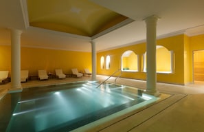 A swimming pool with white columns and sunlit arched windows.