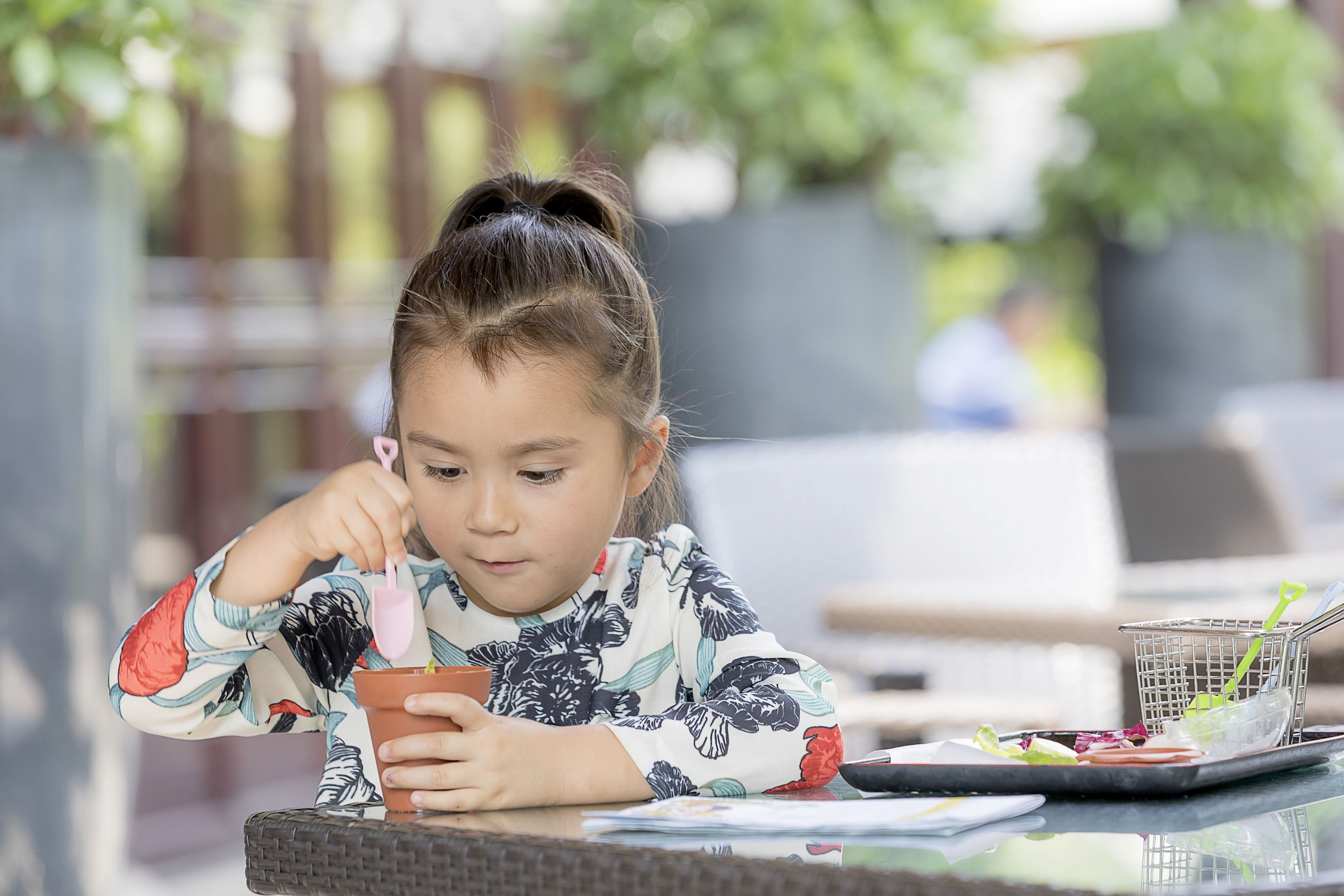 Un enfant mange à une table en plein air, avec un panier de nourriture et une tablette à proximité.