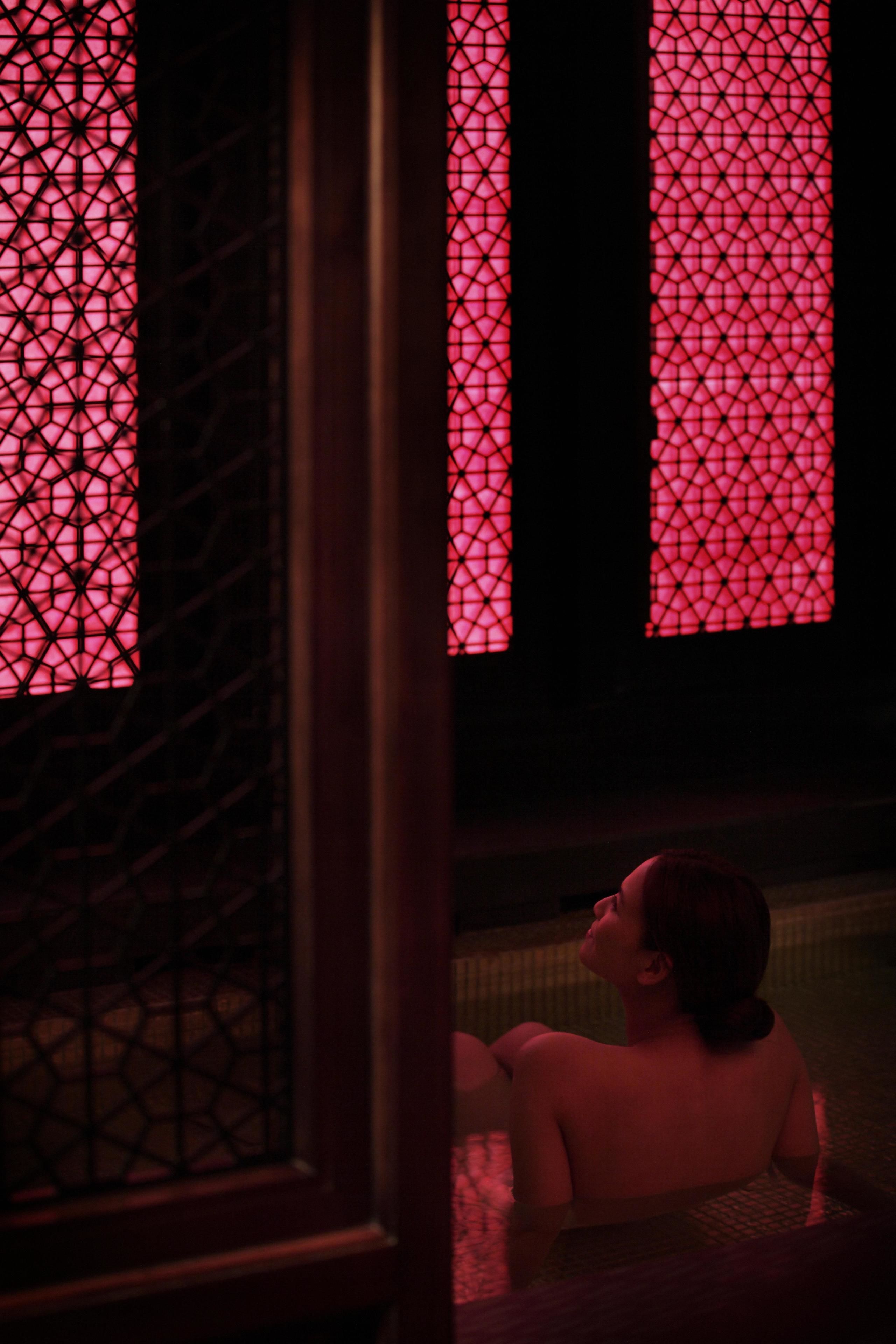 Una persona en una bañera, con una ventana de fondo con diseño geométrico.