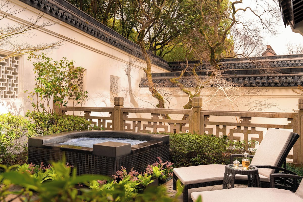A hot tub with a tiled surround, a lounge chair, and a small table with a drink.