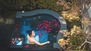 A woman in a hot tub surrounded by rose petals, with a tray of items and a small table beside her.
