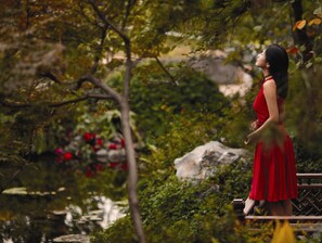 A woman in a red dress standing on a wooden bridge over a pond with red flowers and greenery. - Four Seasons Hotel Hangzhou at West Lake (Hangzhou)