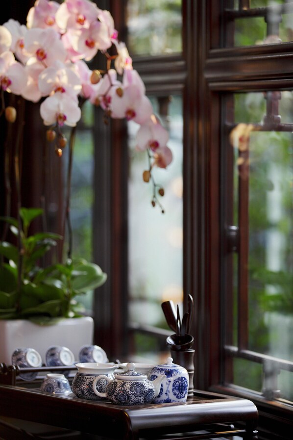 Ventana con vistas a follaje, una planta en maceta y una mesa con teteras y tazas.