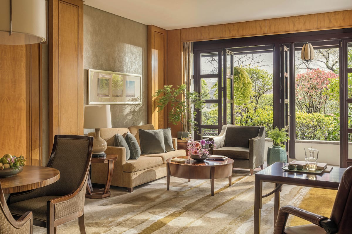 A living room with a sofa, chairs, a coffee table, a dining table, and a large window with a view of trees and a building.
