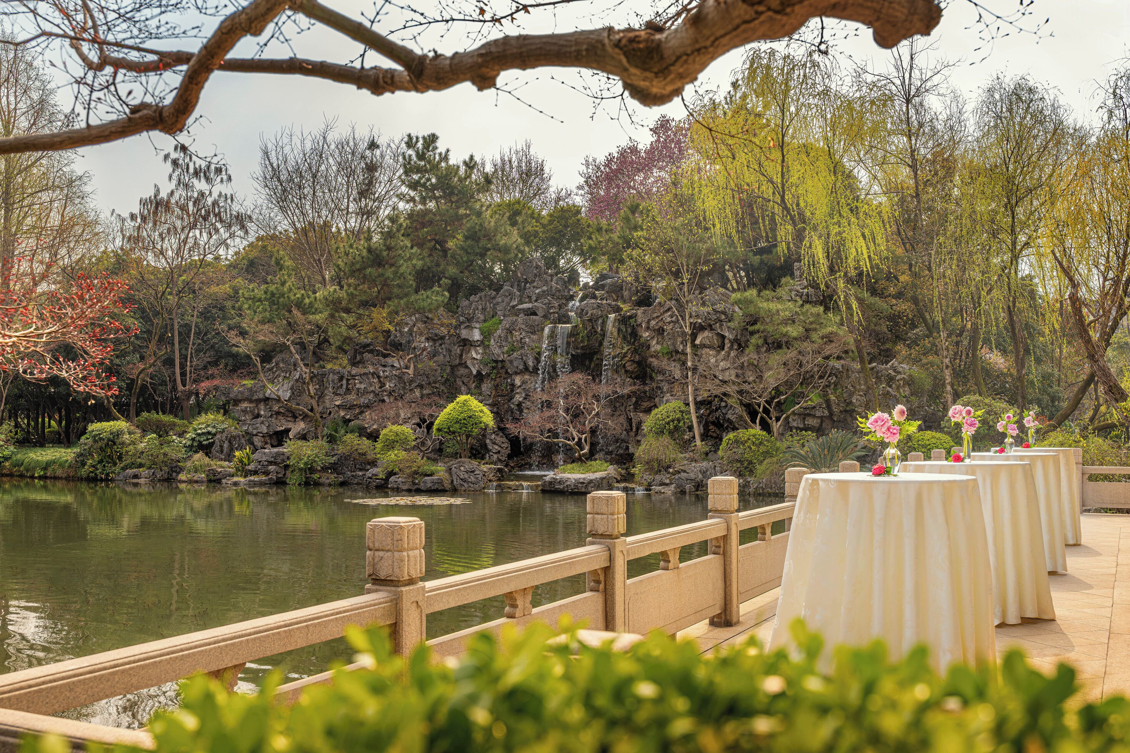 A serene garden with a pond, a wooden bridge, and tables set up for dining.