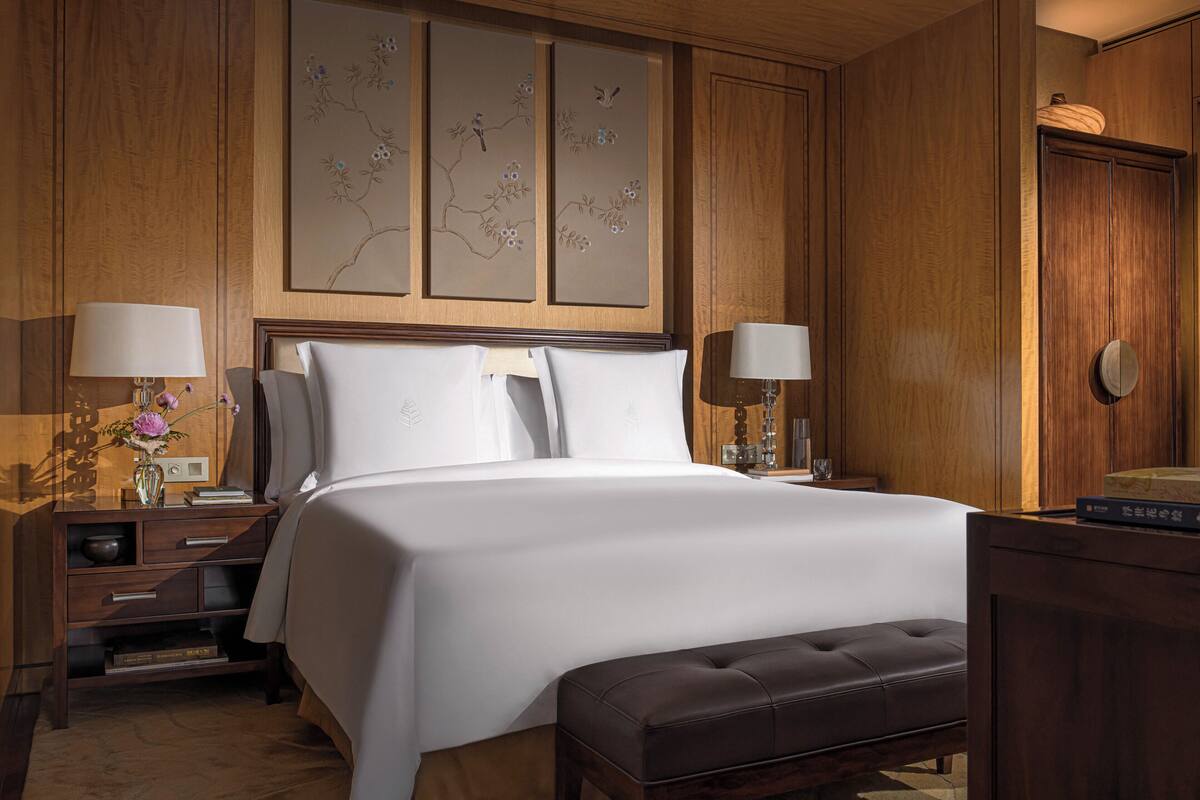 A hotel room with a large bed, two bedside tables with lamps, a wooden wardrobe, and a decorative wall piece.