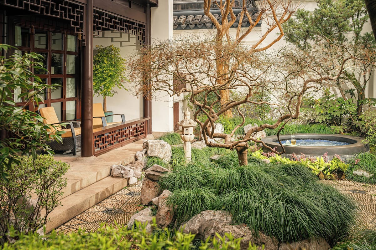 A traditional Japanese-style garden with a stone pathway, a hot spring, and a wooden structure.