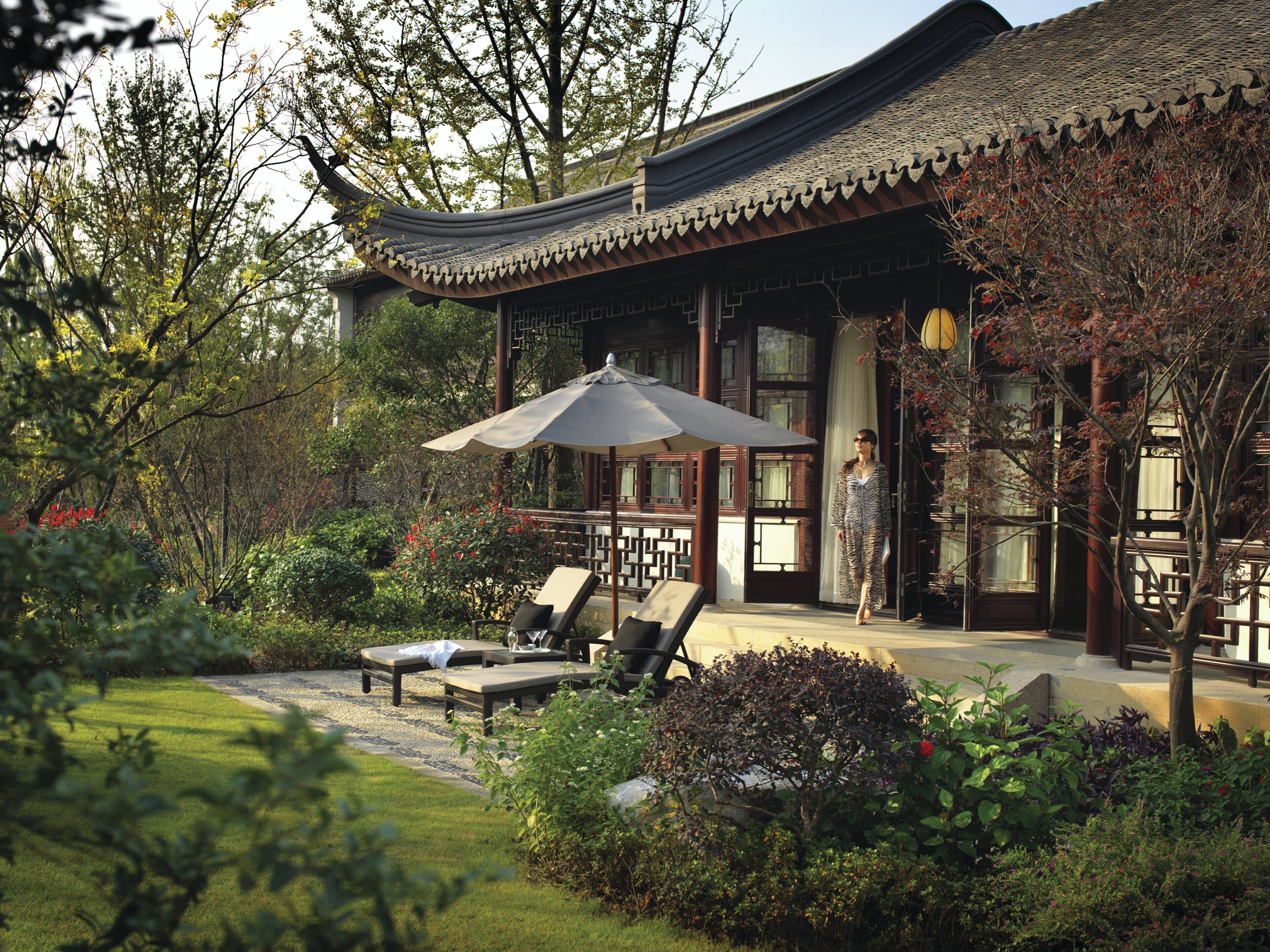 Un bâtiment traditionnel doté d’un toit incurvé, d’un jardin avec un sentier et d’un espace extérieur aménagé avec des parasols.