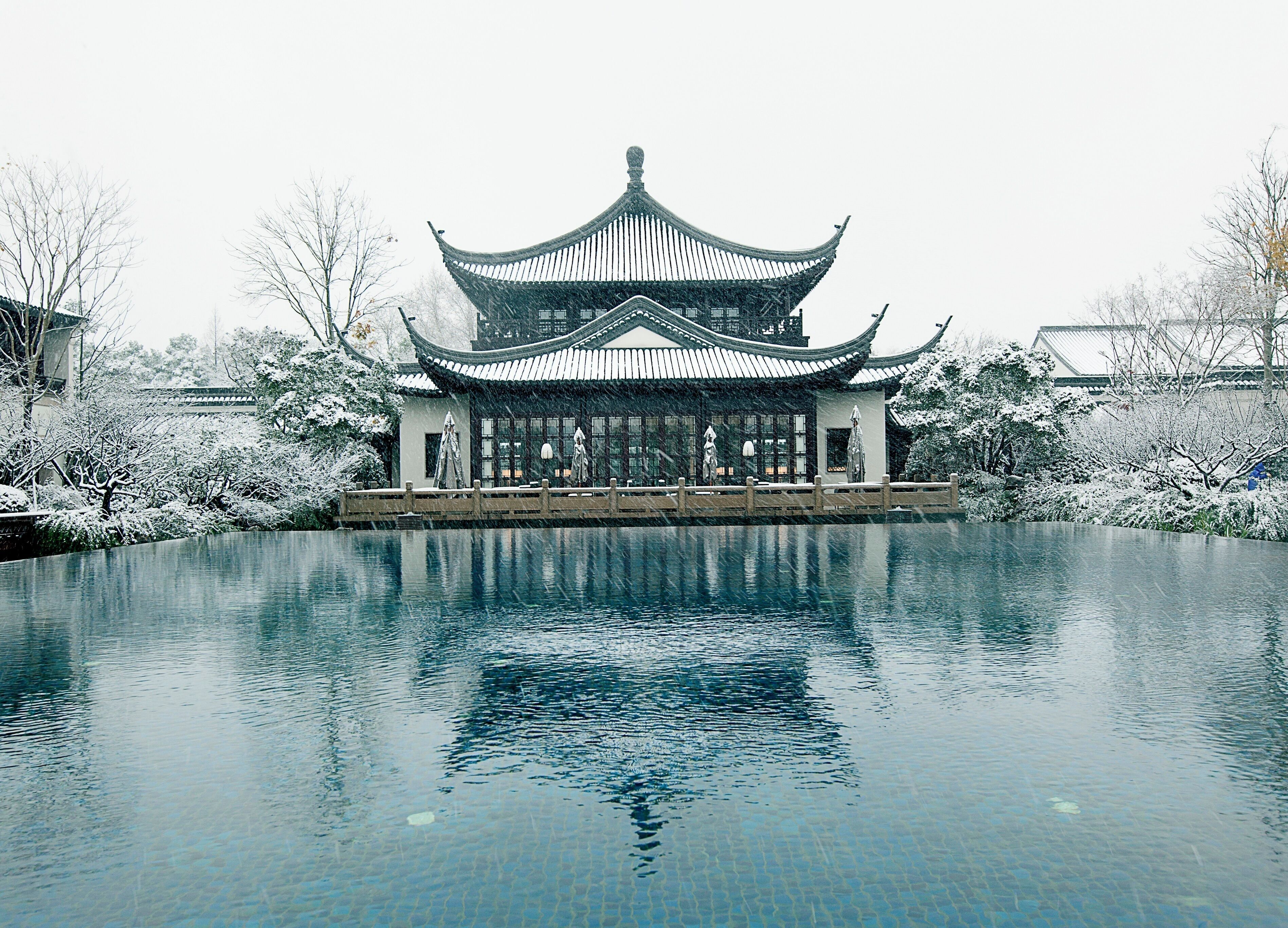 A traditional Chinese building with a symmetrical roof and a reflection in the water in front.