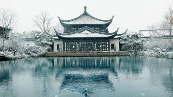 A traditional Chinese building with a symmetrical roof and a reflection in the water in front.