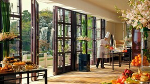 A dining area with a view of a waterfall, a chef preparing food, and a buffet with various dishes.
