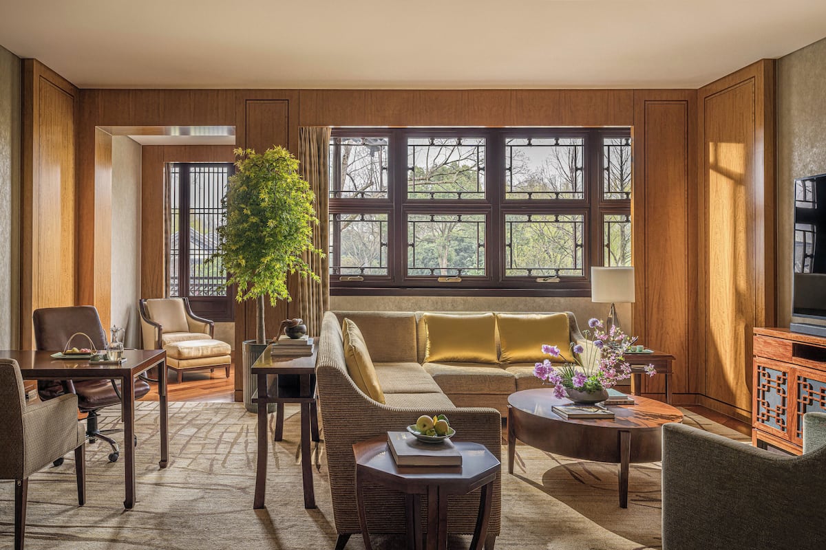 A living room with a sofa, chairs, a coffee table, a TV, and large windows.