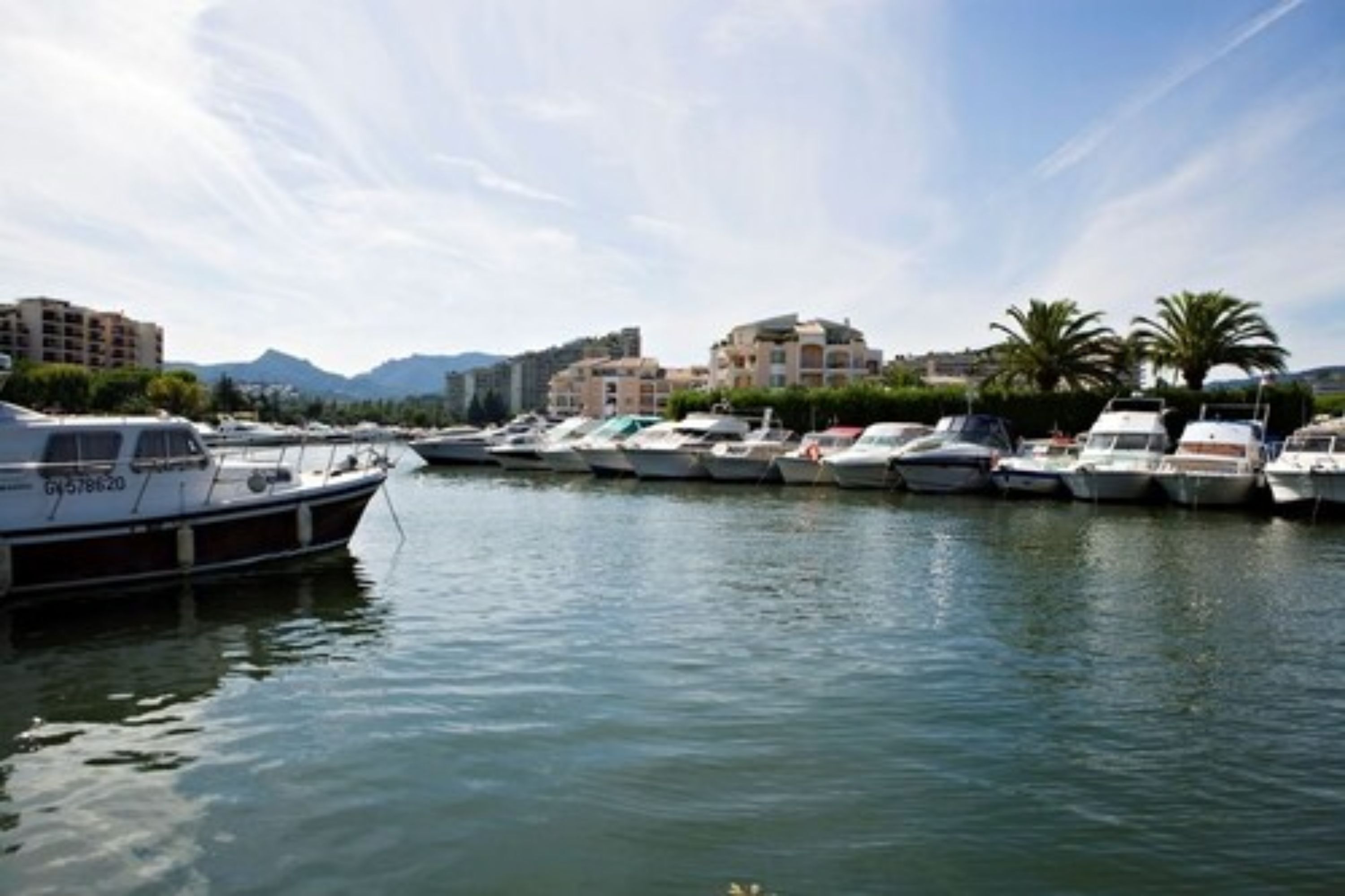 A marina with several boats docked, buildings in the background, and a clear sky.
