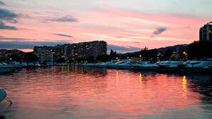 A marina at dusk with boats docked, buildings in the background, and a calm water surface reflecting the sky.