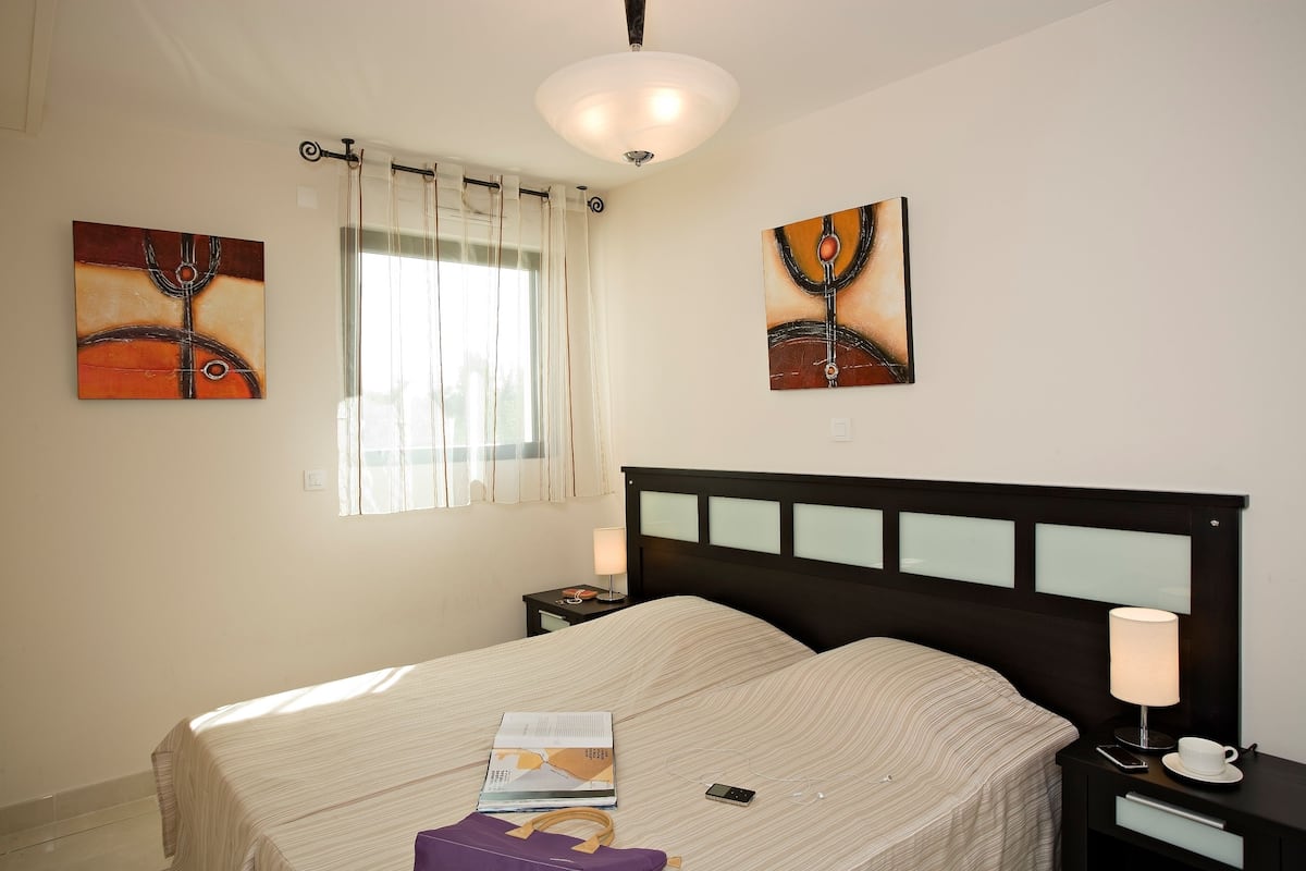 A bedroom with a bed, bedside tables, a lamp, and artwork on the walls.