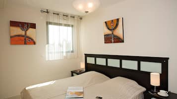 Quarto de hotel com uma cama, uma mesa de cabeceira com abajur e duas pinturas na parede.