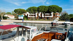 A marina with boats docked, a building with balconies, and a clear sky.