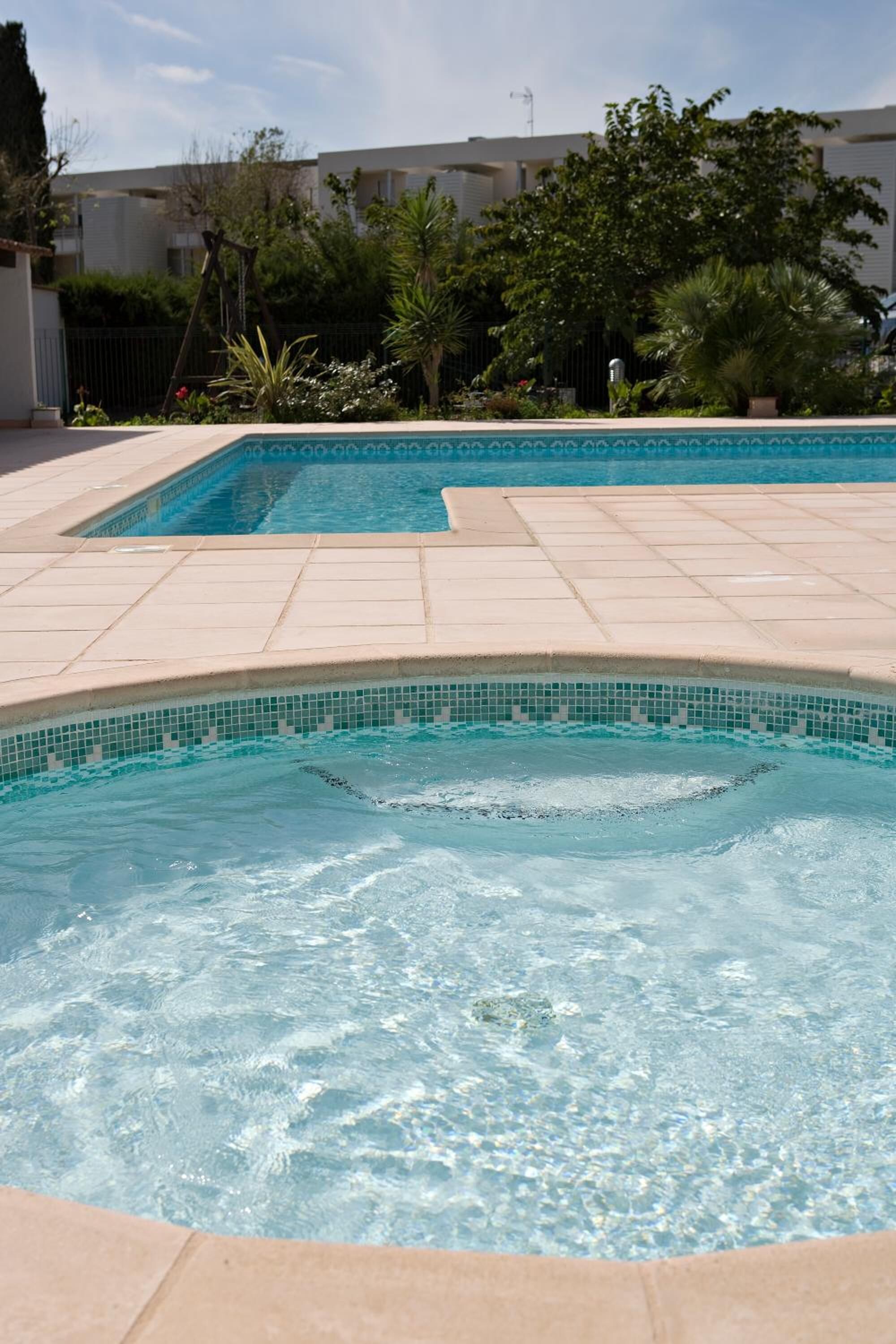 A swimming pool with clear water, surrounded by a tiled deck and greenery.
