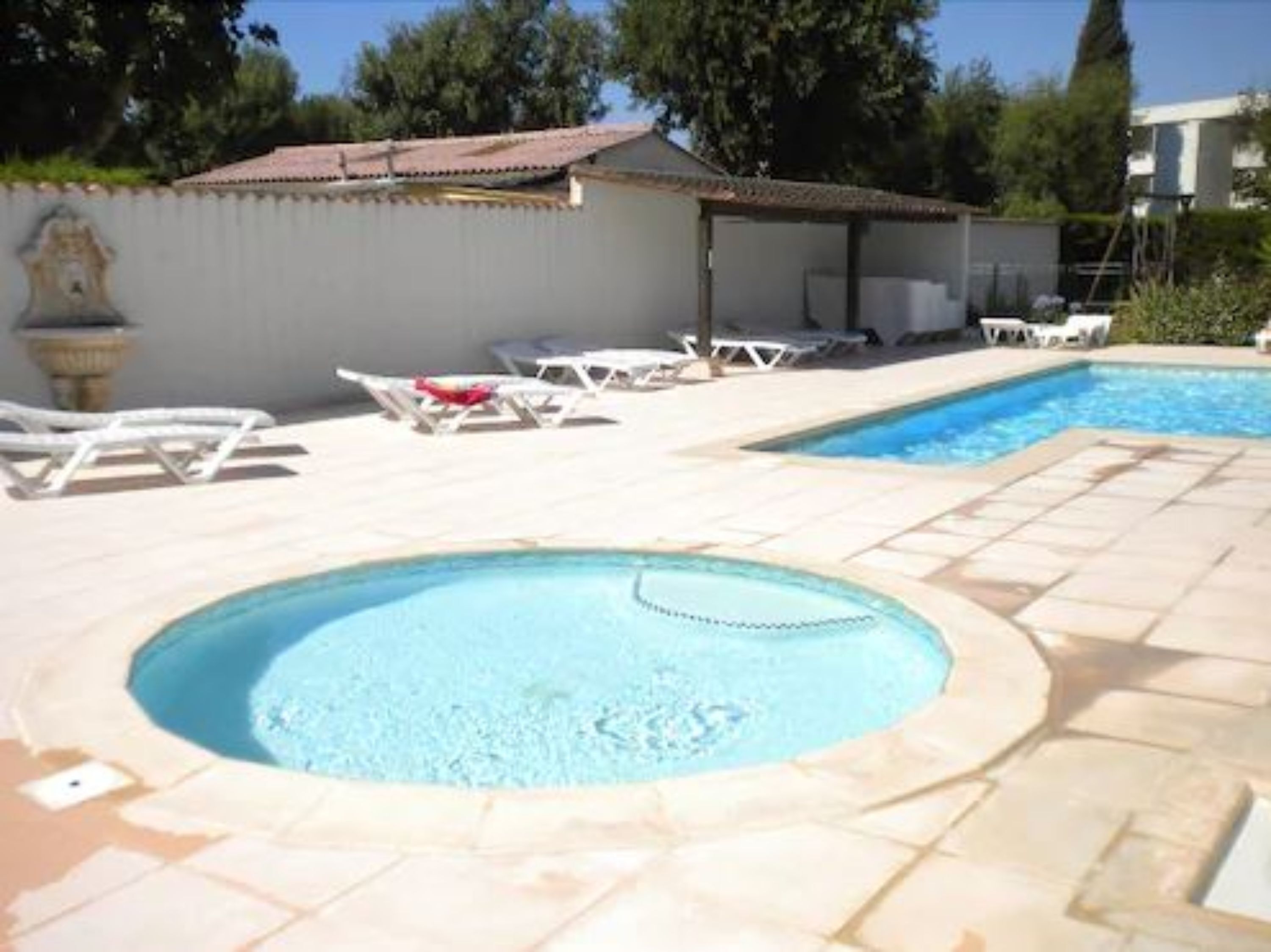 A swimming pool with two separate sections, one with a hot tub, surrounded by lounge chairs and a tiled deck.