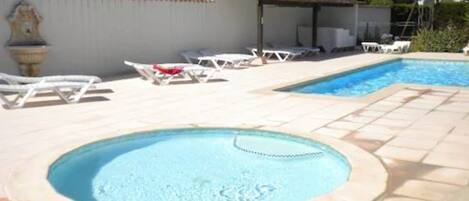 A swimming pool with two separate sections, one with a hot tub, surrounded by lounge chairs and a tiled deck.
