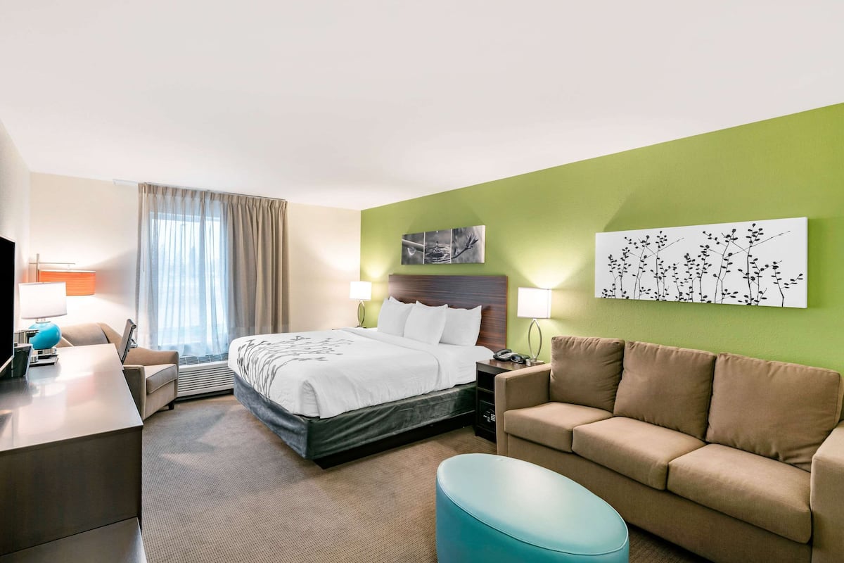 Ein Hotelzimmer mit Bett, Schreibtisch, Sofa und Fernseher.