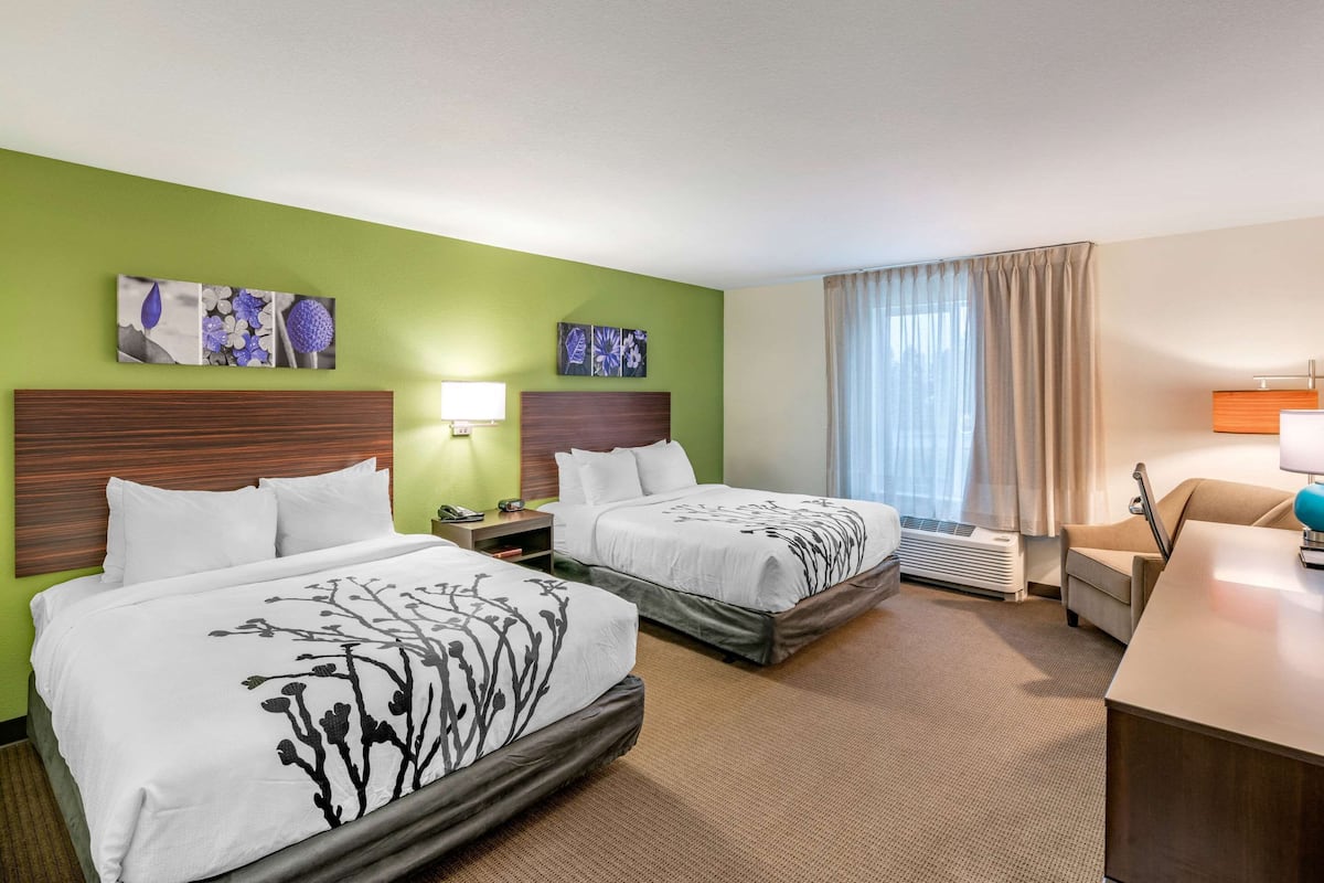 Ein Hotelzimmer mit zwei Betten, einem Schreibtisch, einem Stuhl und einem Fenster mit Vorhängen.