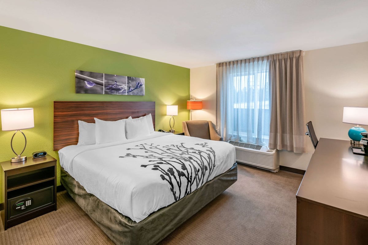 Ein Hotelzimmer mit Bett, Nachttischlampen, einem Schreibtisch und einem Fenster mit Vorhängen.
