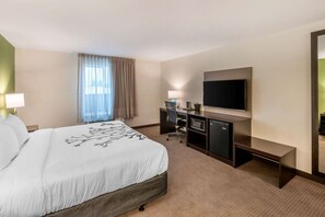 A hotel room with a large bed, a desk with a computer, a flat-screen TV, and a large mirror.