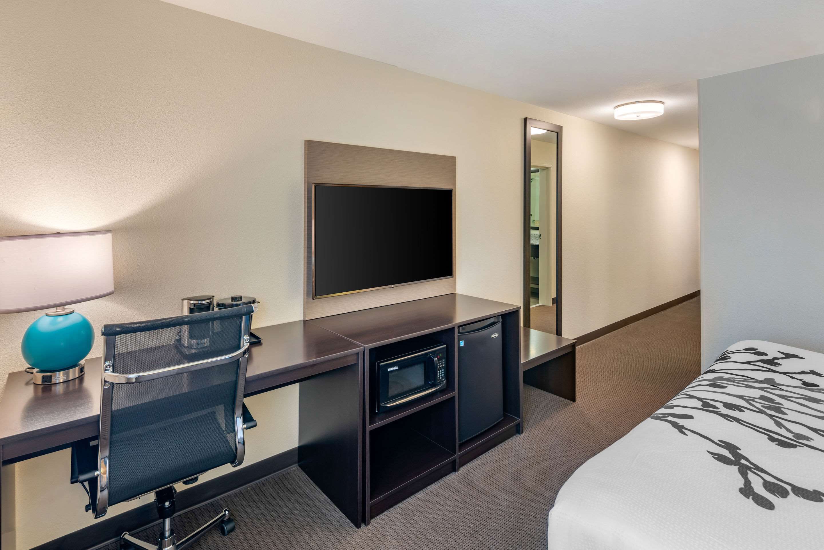 Une chambre d’hôtel équipée d’un lit, d’un bureau avec un ordinateur, d’un four à micro-ondes, d’une lampe et d’une télévision.