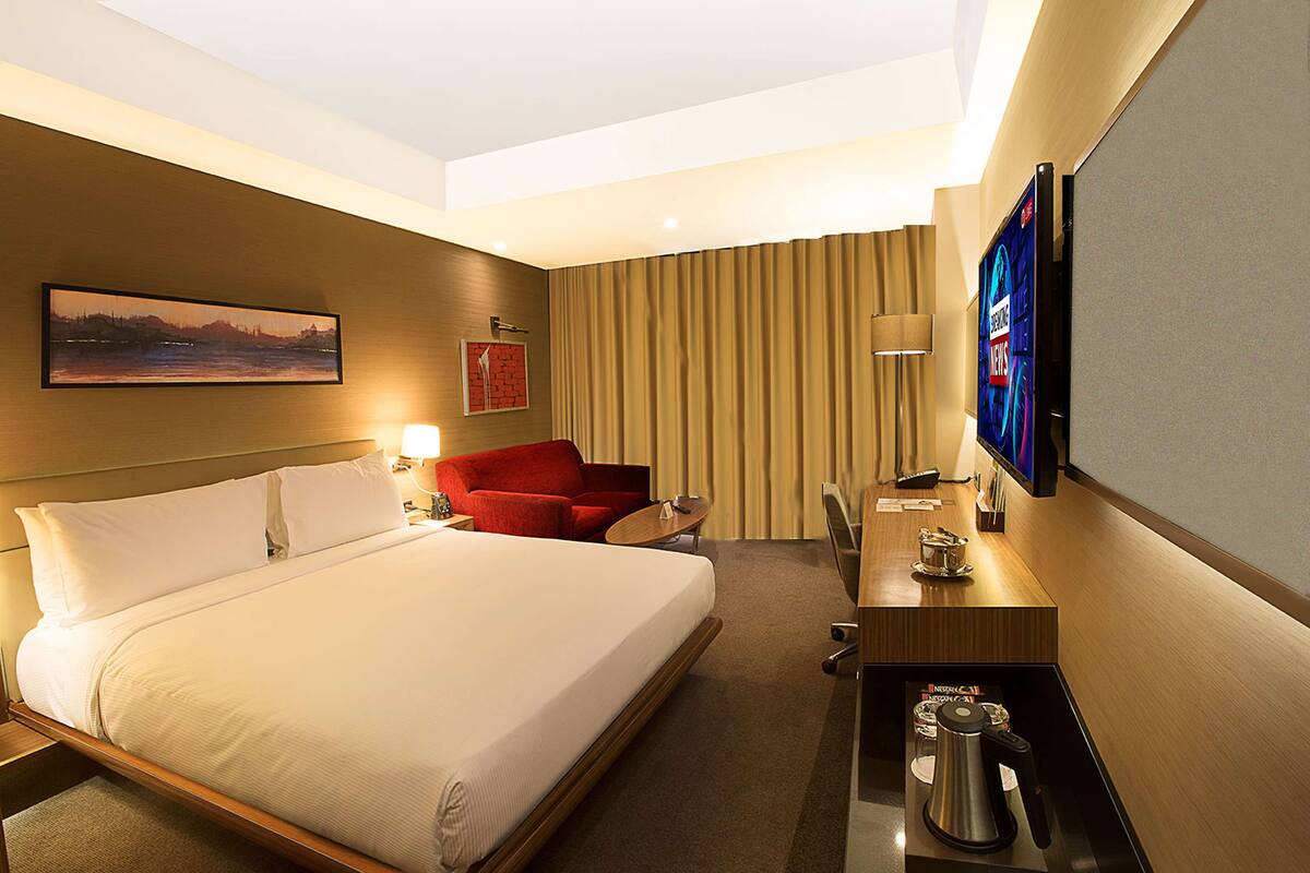 A hotel room with a large bed, a desk with a coffee maker, a TV, and a red chair.