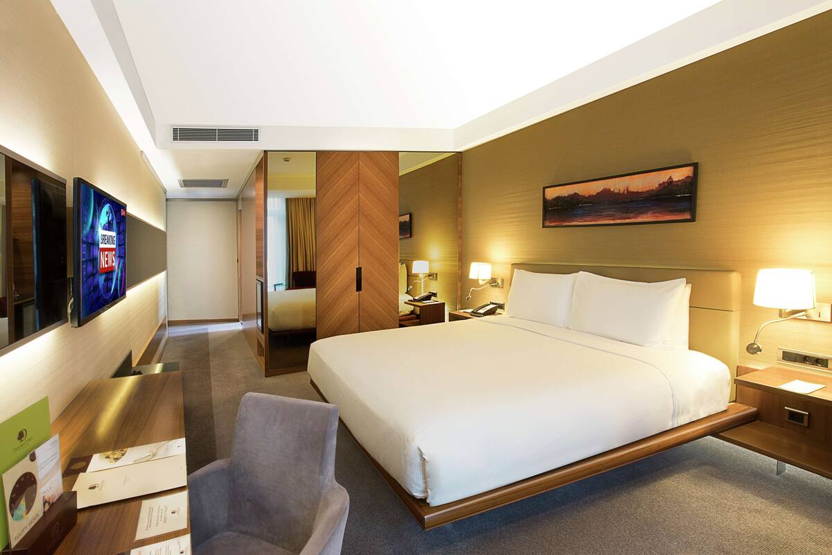 A hotel room with a large bed, bedside tables, a desk with a chair, a TV, and a painting on the wall.