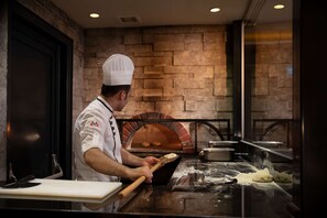 A chef preparing dough in a kitchen with a brick oven and stone walls. - Doubletree By Hilton Istanbul Old Town (Istanbul)