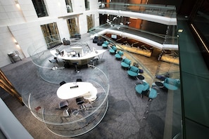 Ein mehrgeschossiges Atrium mit einer zentralen, offenen Besprechungsfläche, Sitzgelegenheiten und einem Empfangsbereich.