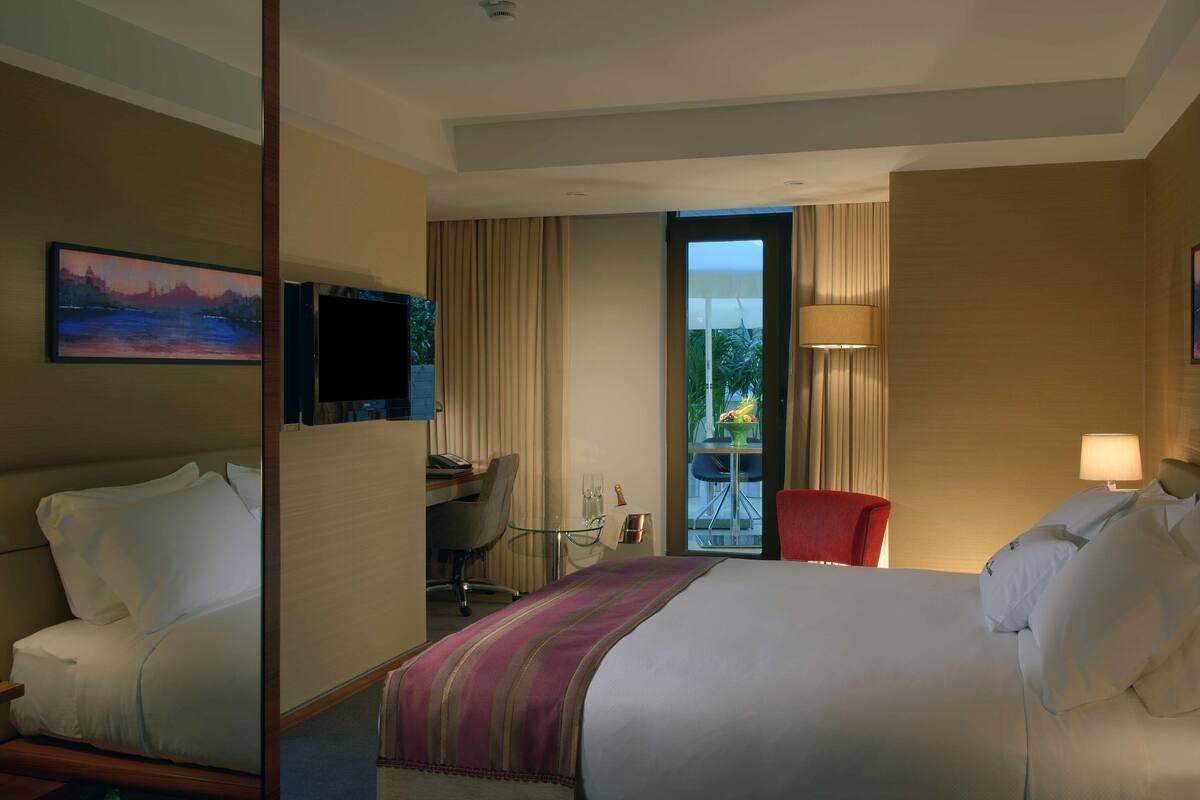 A hotel room with a bed, a desk with a chair, a TV, and a window with curtains.