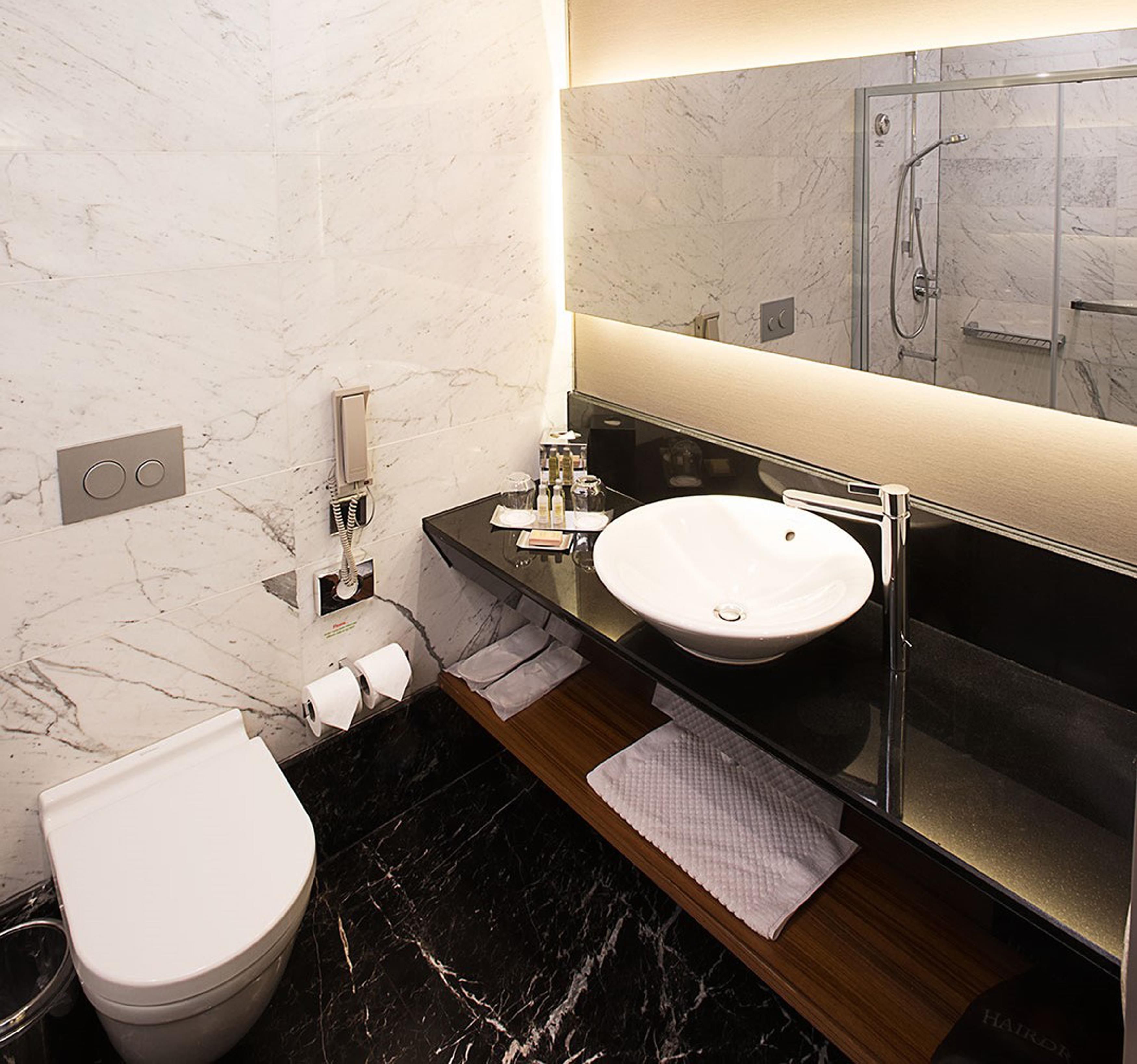 A modern bathroom with a marble wall, a white toilet, a vanity with a sink, and a shower area.